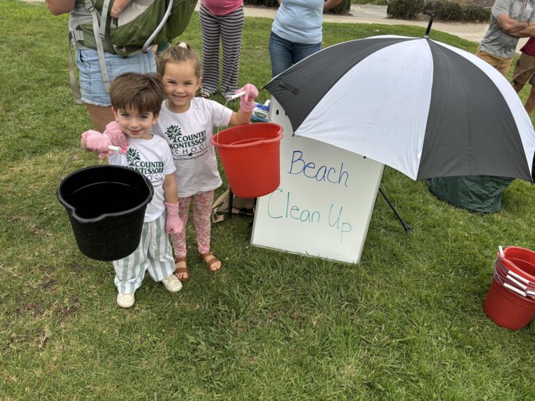Two young students with buckets next to a "Beach Clean Up" sign at Fletcher Cove