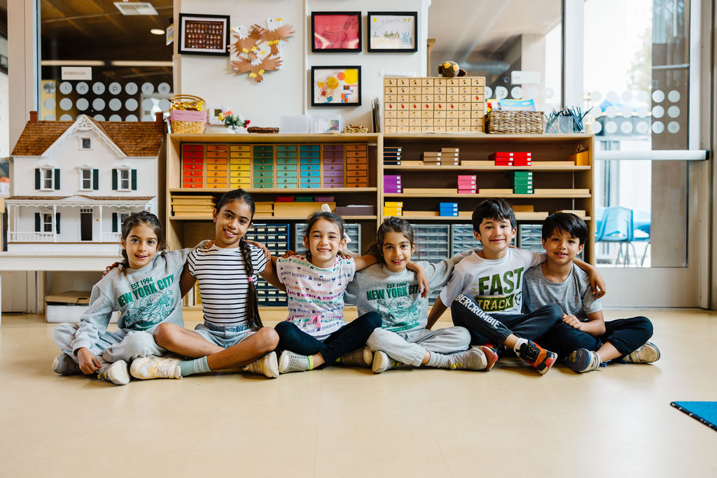 Six smiling students sitting together on the floor of a Montessori classroom at Country Montessori School in Poway