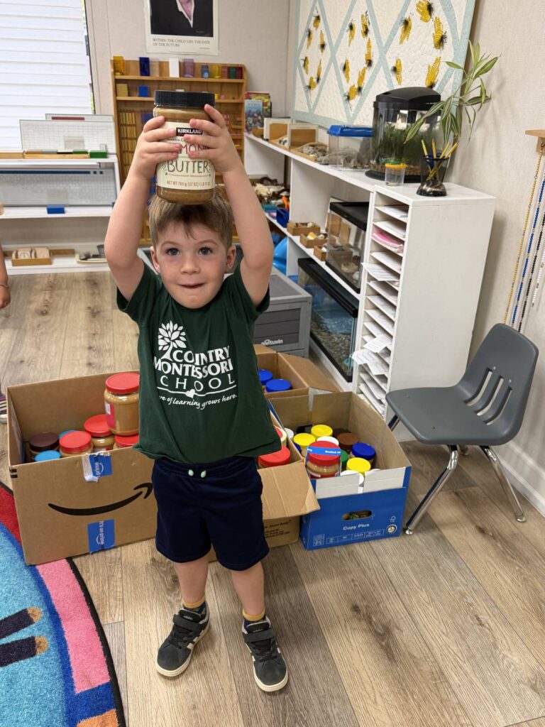 Student holding a jar of peanut butter over his head next to the class donation box