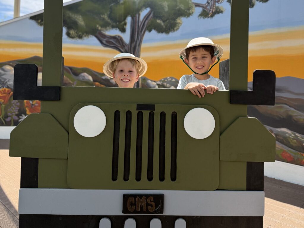 Two smiling campers in safari hats looking out of the CMS jeep photo booth at summer camp in Poway